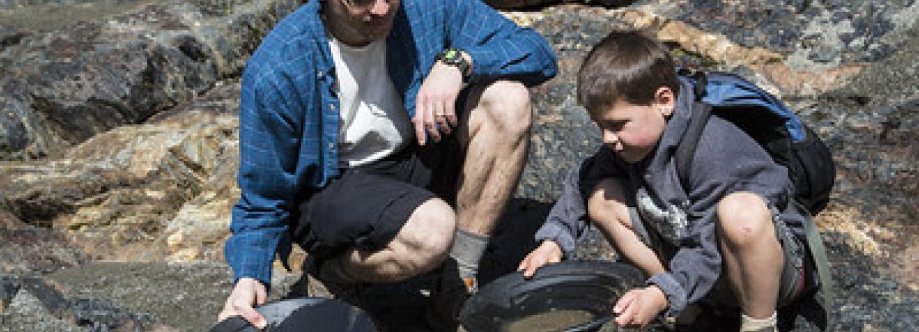 A Father and sun gold pan next to a forest river.