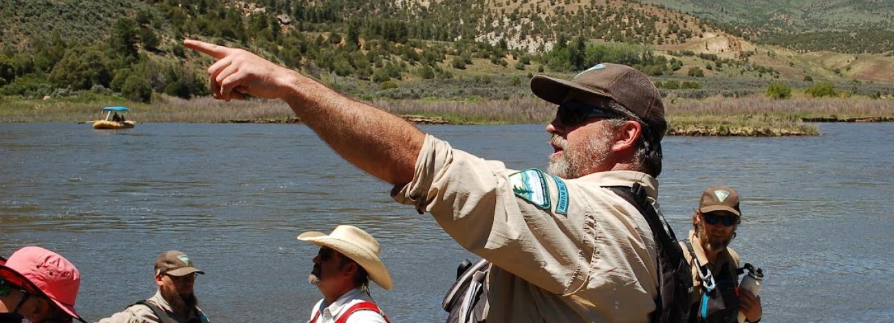 BLM employee pointing in the distance with the Colorado River and four other people in the background of the image. 