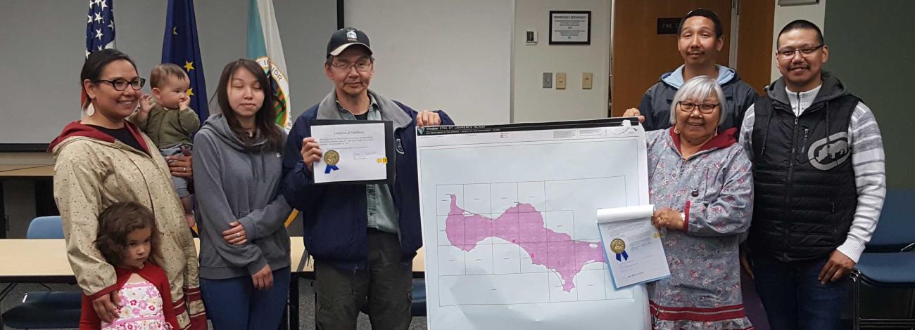 Alaskan family stands in front of a map holding certificates.