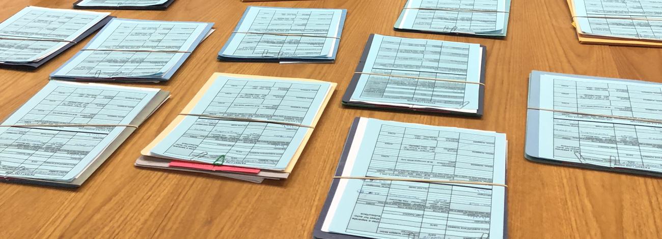 Singular folders with blue papers on top are banded and spread out on a wooden table.