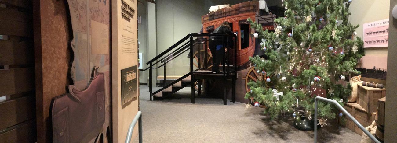 Christmas tree in foreground with a covered wagon behind it. 