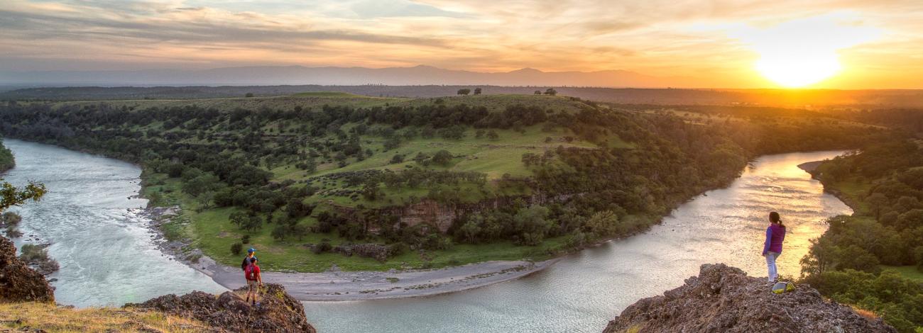 People overlook a river at sunset