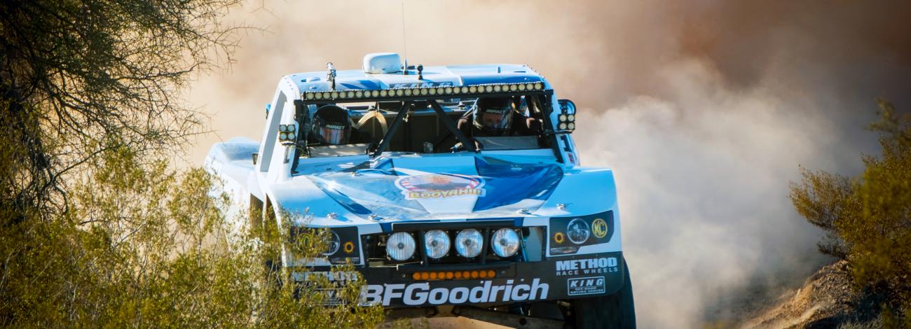 A blue truck drives through the dirt.