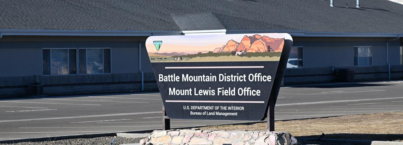 With a blue sky and snow-capped mountain in the background, a Bureau of Land Management sign sits in front of the Battle Mountain District Office which includes the Mount Lewis Field Office. 