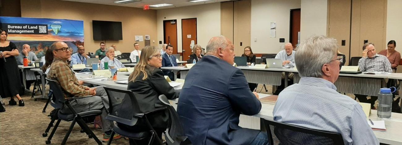 Large meeting room-Members of an advisory council are seated at a long table. 