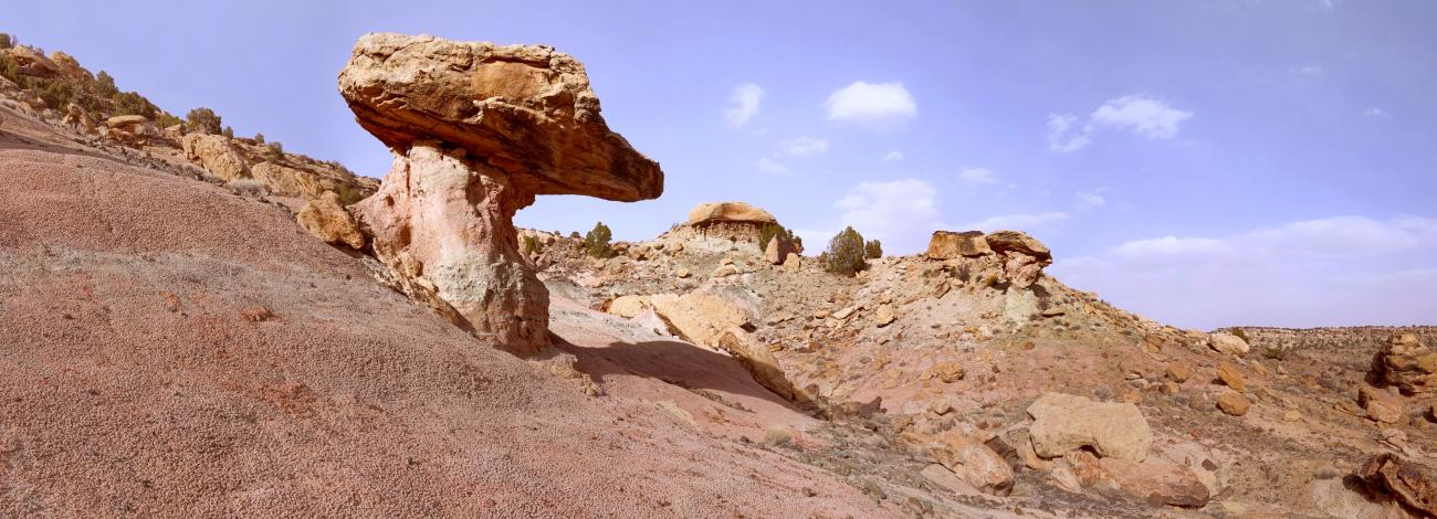 Sloped red rock with mushroom shaped rock eroded from the bare rocky landscape