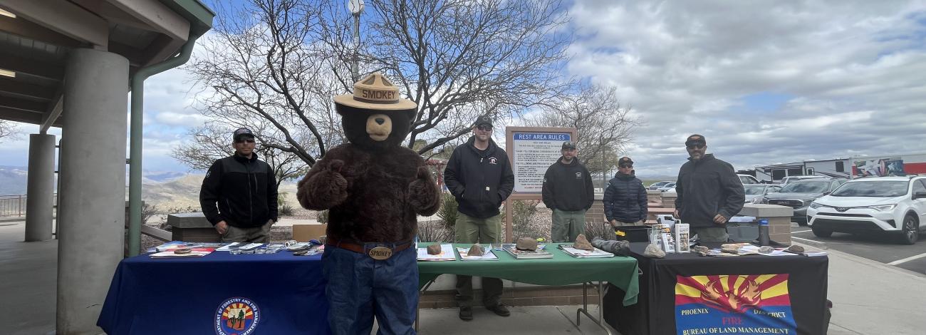 Wildfire prevention experts and Smokey Bear at an event Sunset Point Rest Area. It is a partly cloudy day.