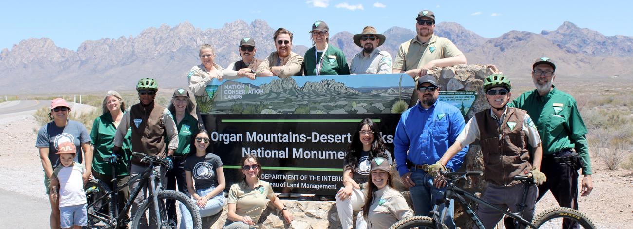 The Organ Mountain Desert-Peaks team posing in front of the monument portal sign for the tenth anniversary celebration.
