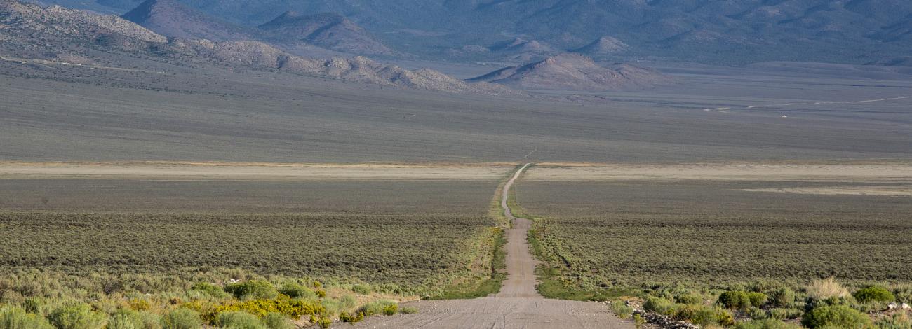 A gravel access road leading to a mountain range.