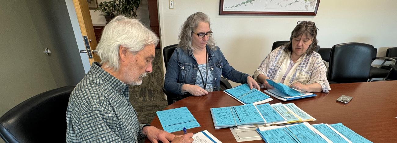 Three people at desk, one signing a document