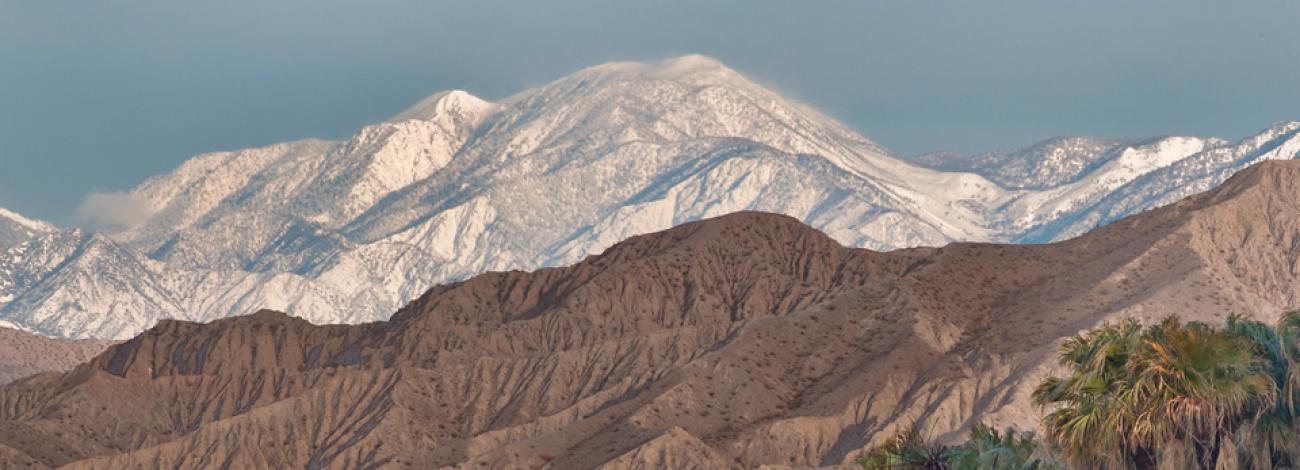 Bare desert hills in the foreground with snow capped peaks in the background.