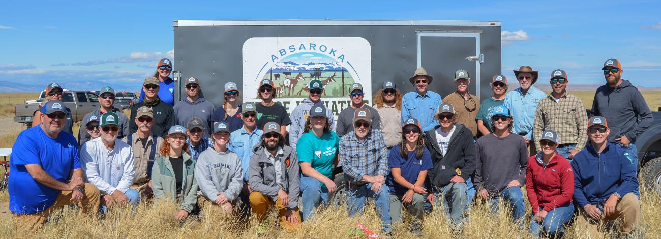 A group of about 40 people gather for a photo in front of a trailer with a banner on the side that says "Absaroka Fence Initiative".