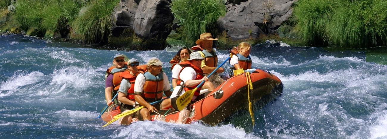 group of folks in personal flotation devices floating on the river in a boat
