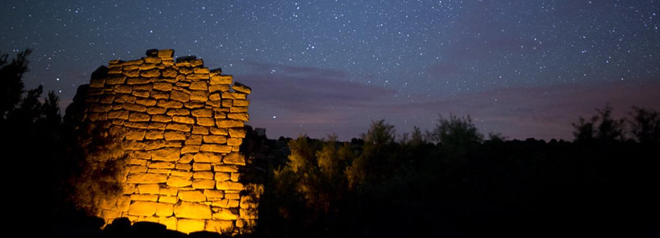The Milky Way is visible over a dark mountain valley with illuminated ruins perched above