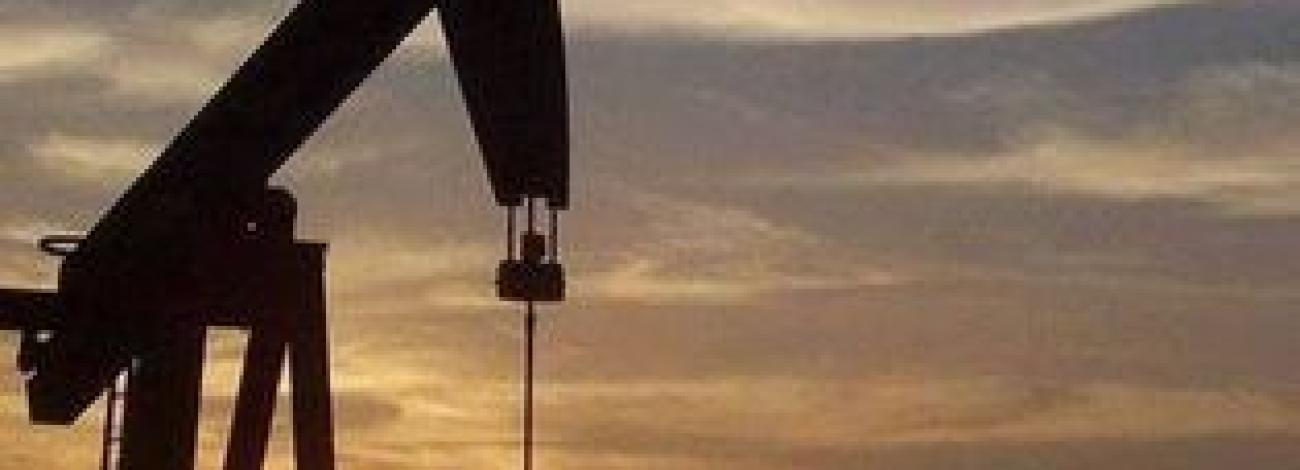 an oil rig is backlit by the sun setting in a cloudy sky