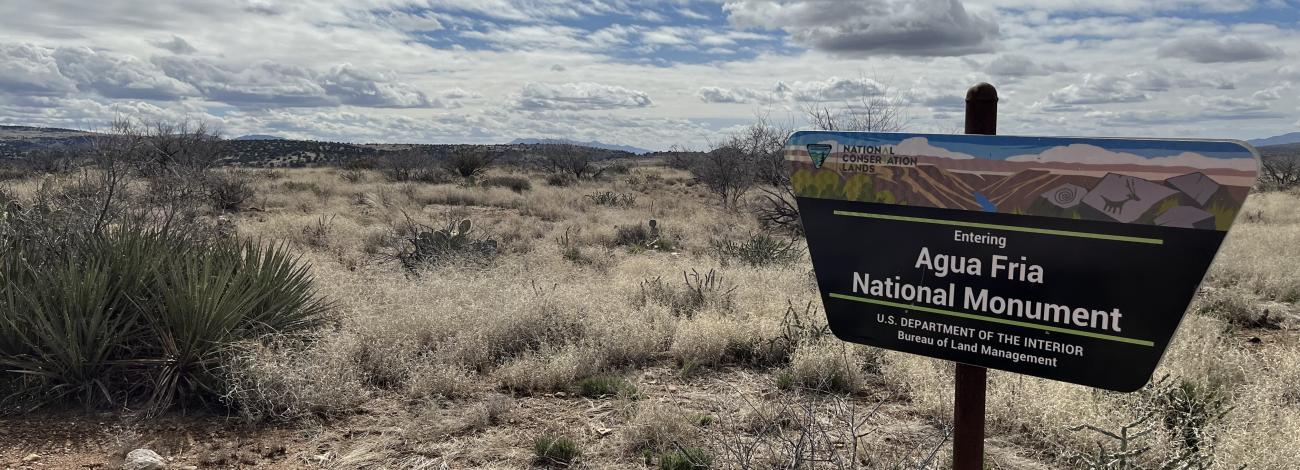 in a desert landscape, a trapezoid shaped sign says Agua Fria National Monument, US Department of the Interior, Bureau of Land Management