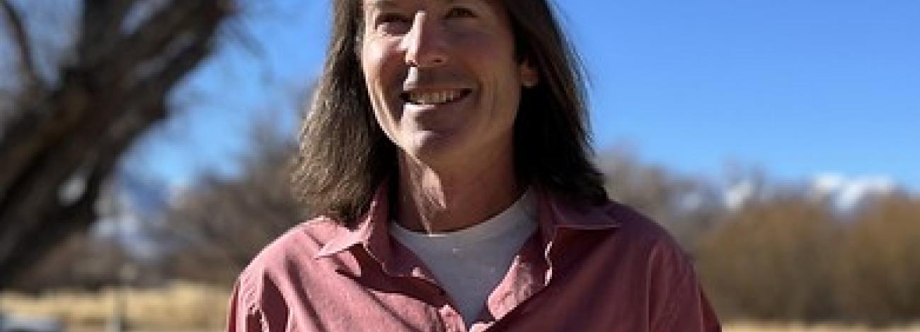 Neal Craig stands outside on a blue sky day with blurred tree in the background