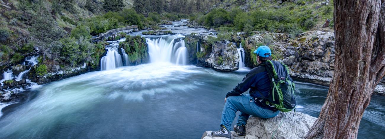 A man sits and looks at a waterfall at Arkansas River from the rocky edge of the river.