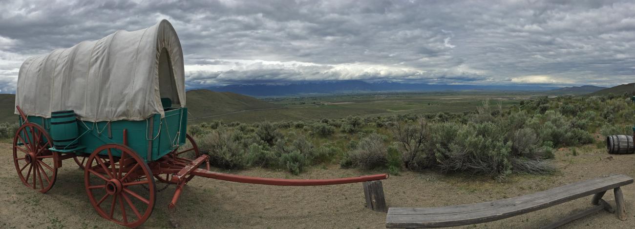 A panorama image of a pioneer-style wagon that is perched next to a simple wooden bench.
