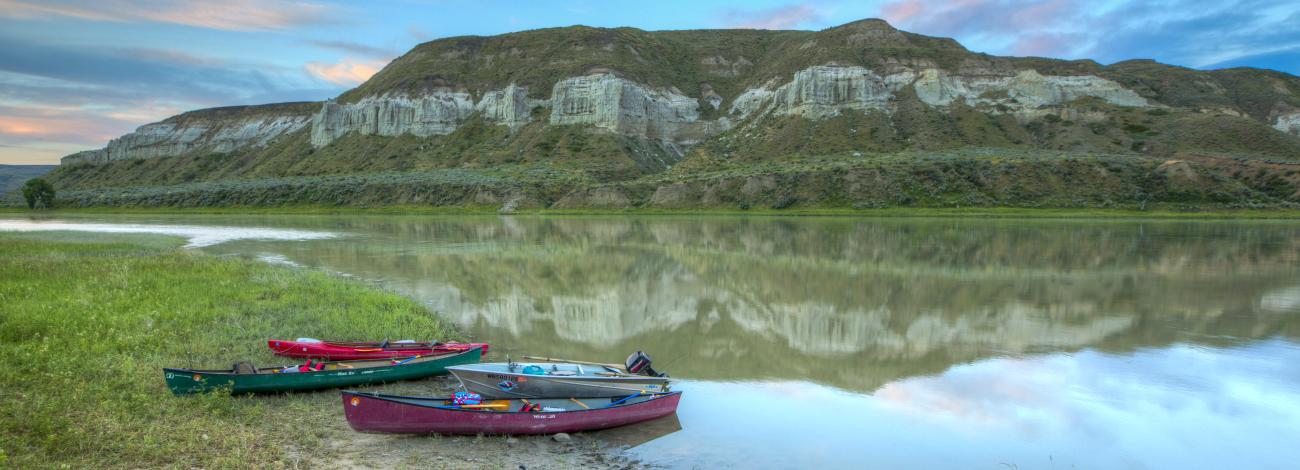 Five canoes are laid out on the bank of a river.