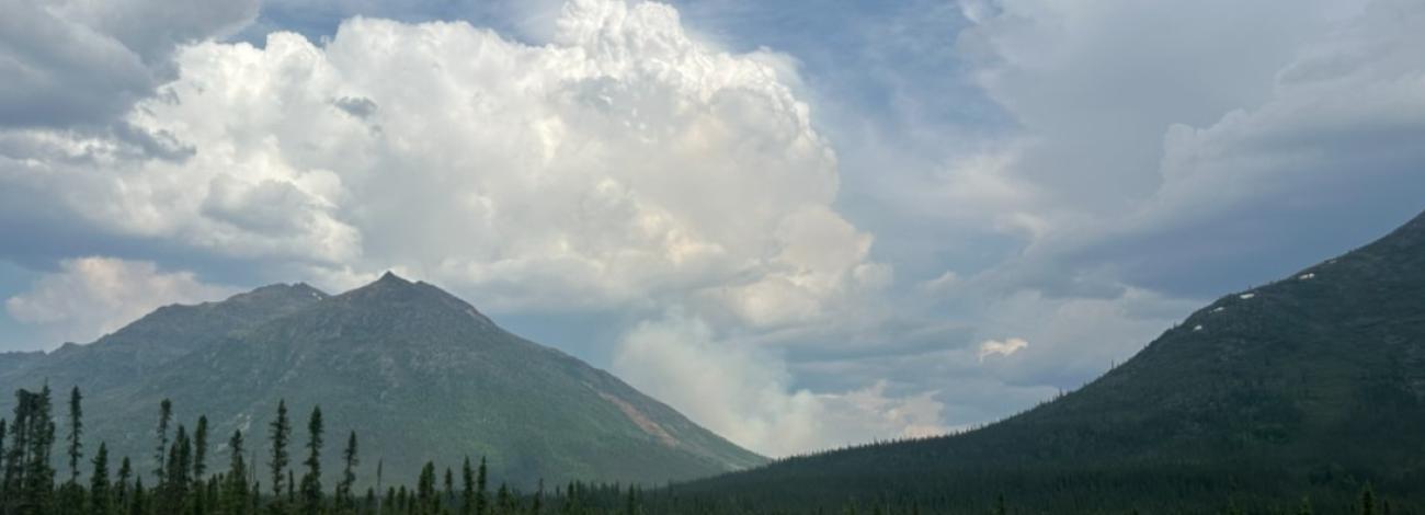 A cloud of smoke rises above the mountain valley.