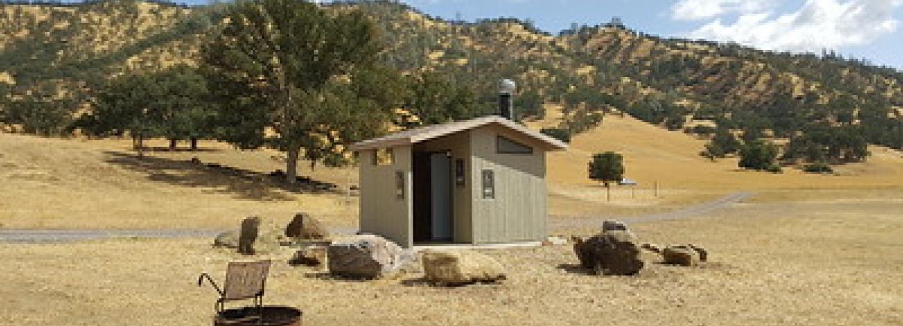 A dry campground with a vault toilet and a fire ring