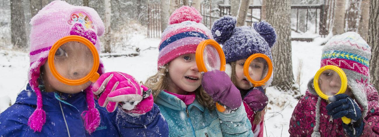 Kids in a snowy forest look through magnifying glasses
