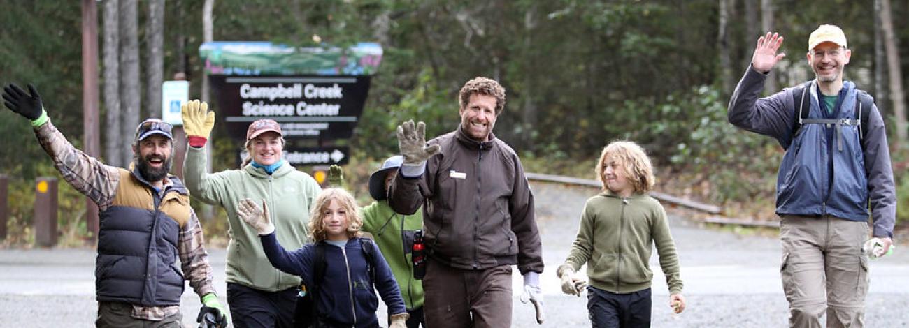 Volunteers wave as they walk down the road wearing work gloves.