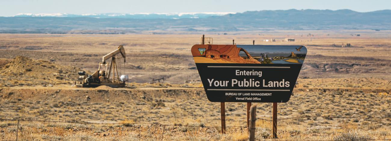 A sign that says "Entering Your Public Lands" In the foreground with an oil derrick in the background on BLM lands