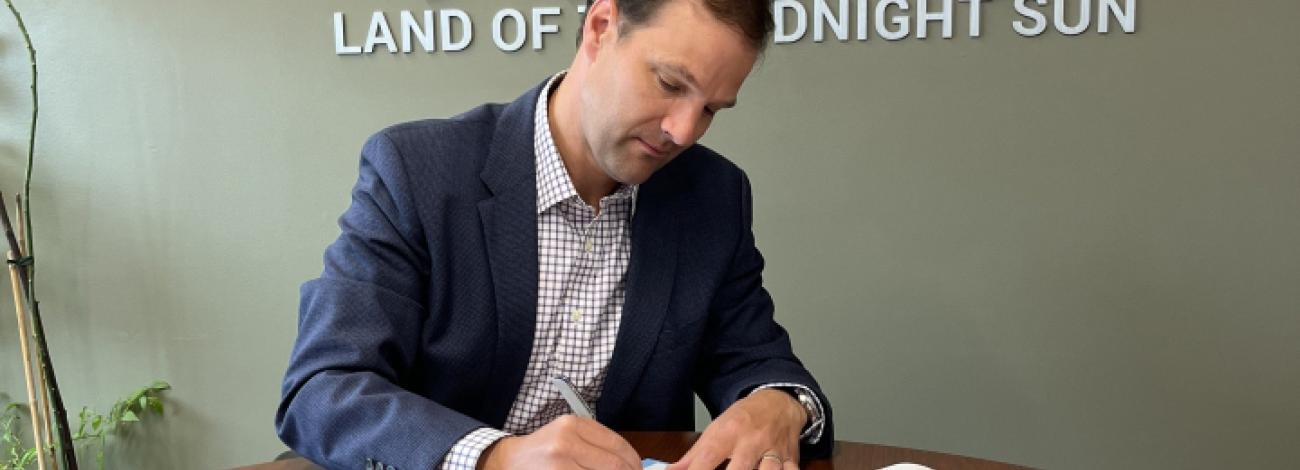 A man sits at a conference table signing a multi-page document.