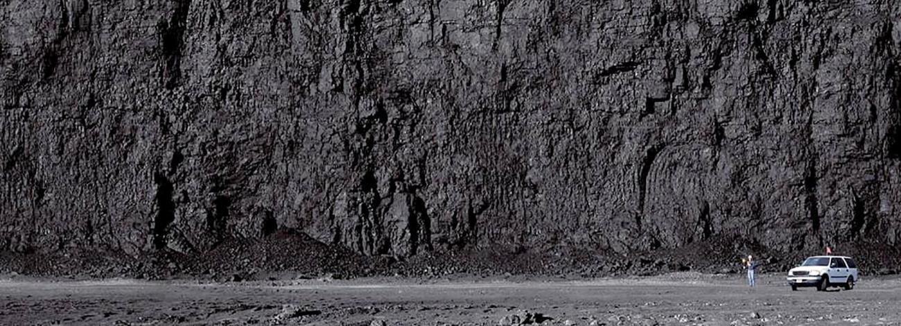 Huge coal wall at the Powder River Basin with worker wearing hardhat and truck at the base of it in Wyoming