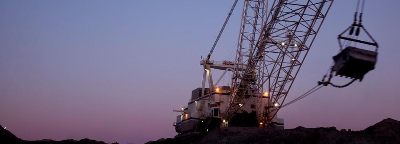 A dragline is silhouetted against a purple and blue sky at an open pit coal mine.