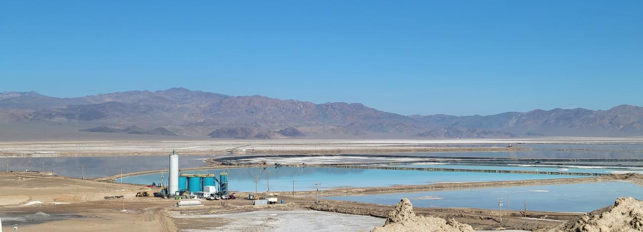 Towers and other mining related structures are alongside manmade ponds with mountains in the background.