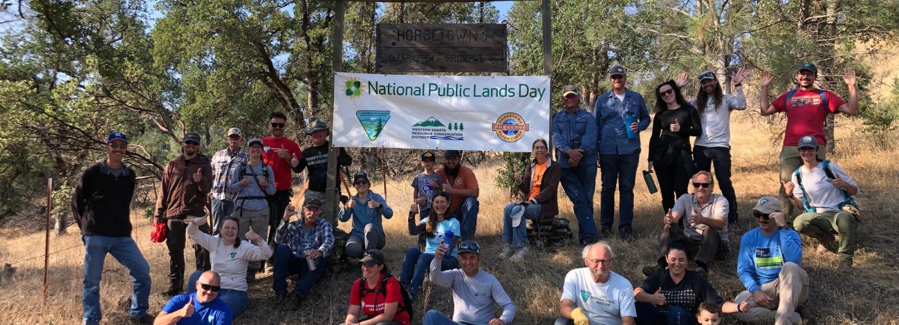 Group of volunteers sit on a dry grassy hill near a npld sign
