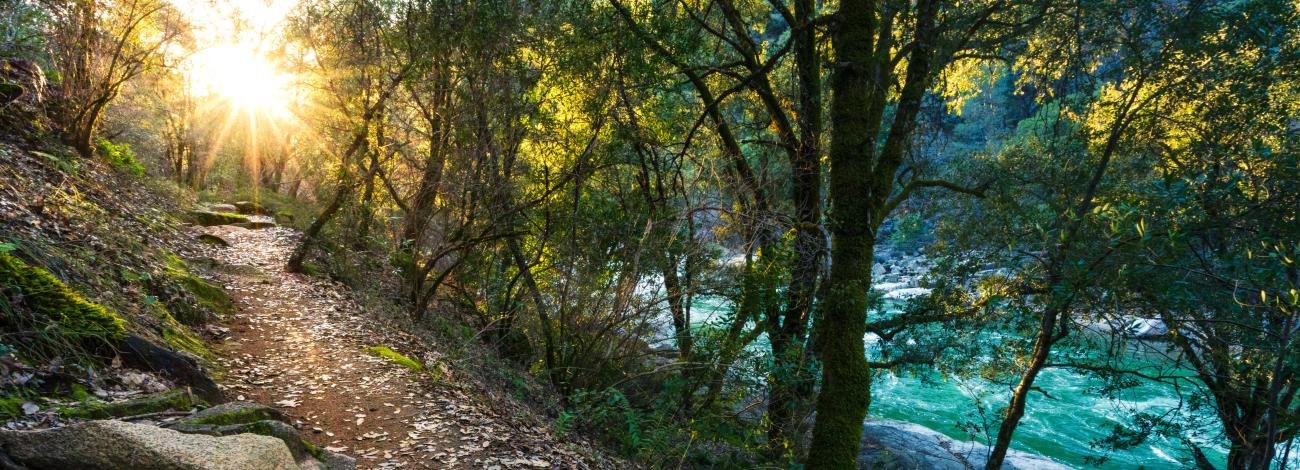 The sun set s over a trail and a clear, blue river.