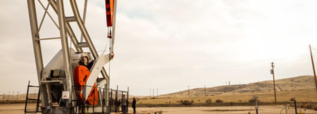 A white and red pump jack rises over dried grass hills.