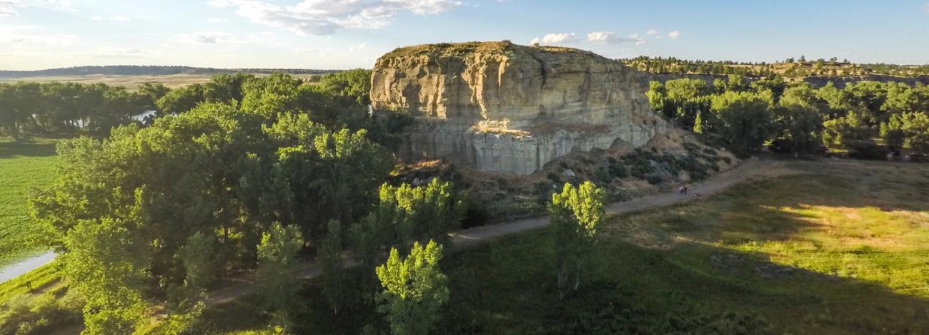 Aerial view if a large rock formation surrounded by green trees and a path along one side.