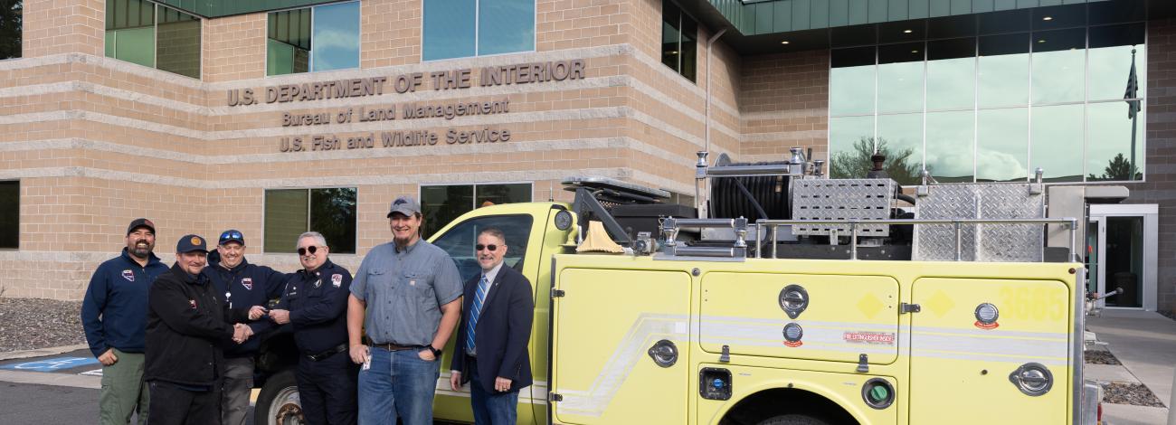 Group of people stand in front of a yellow fire engine, looking at the camera and smiling. 