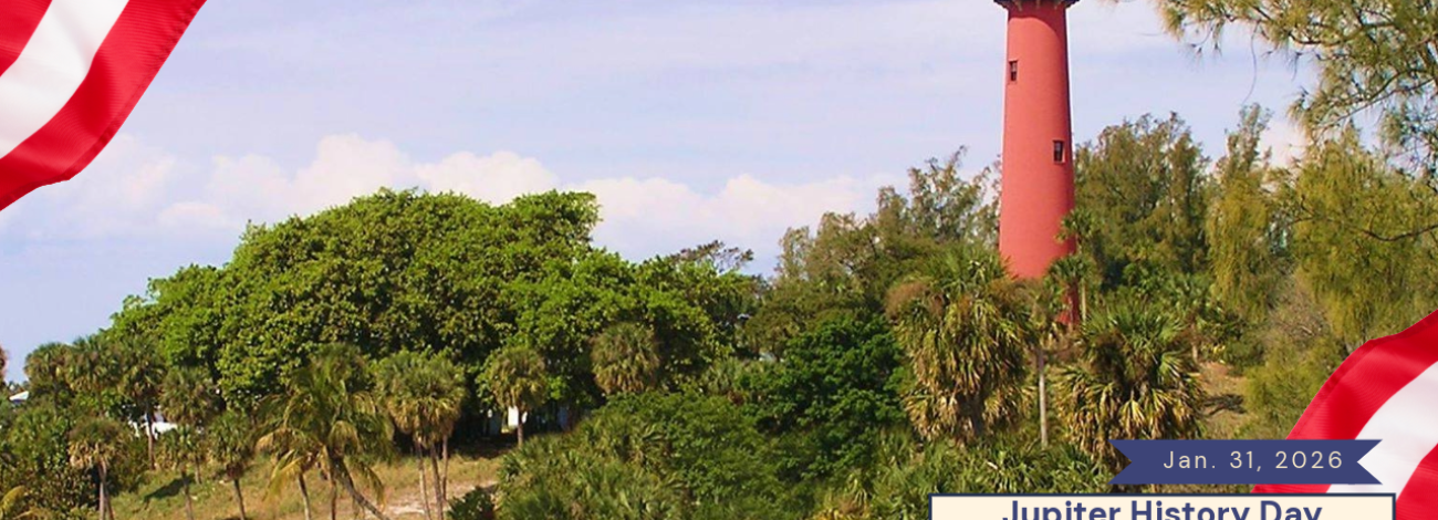 Tall red lighthouse surrounded by green trees under a clear sky with American flags framing the scene for Jupiter History Day Festival.
