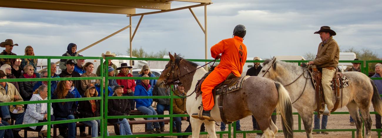 Two men ride horses in front of a large crowd