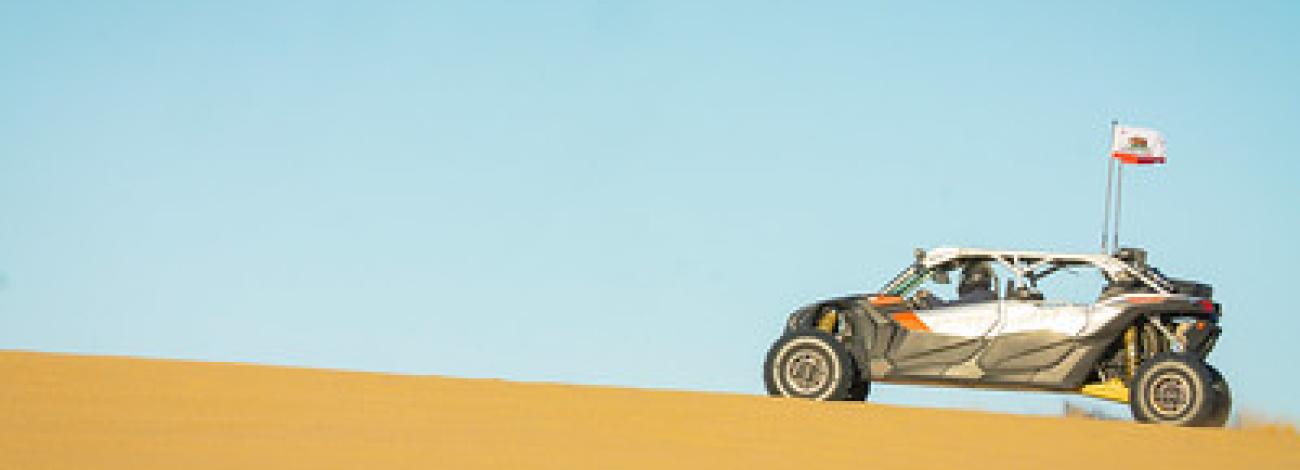 An off road vehicle ascends a gradual dune.