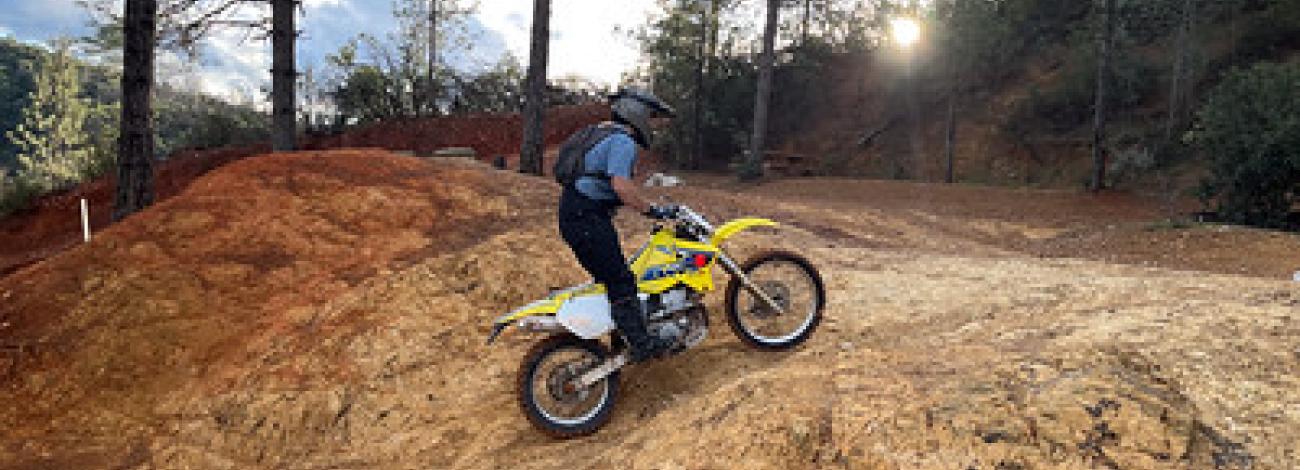 A dirt bike rides up a brown hill in the forest.