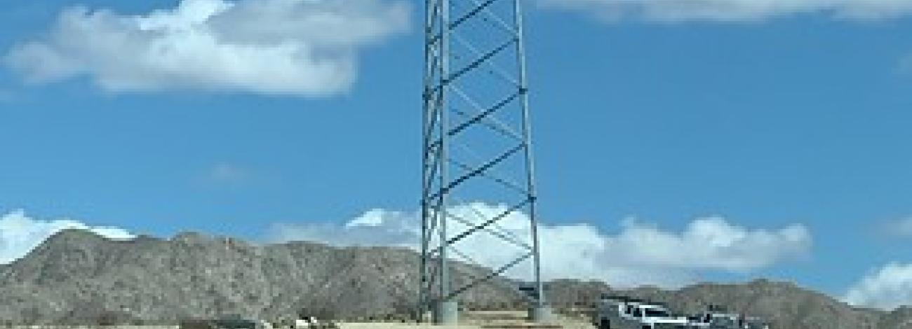 A tall communications tower rises over a desert landscape.