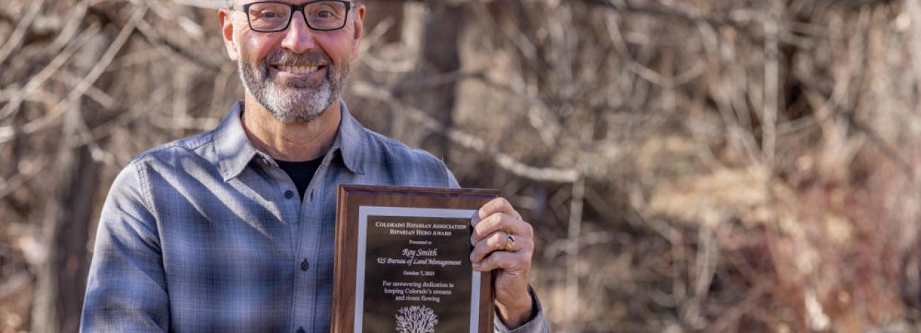 A man holds a placard in a field with trees in the background