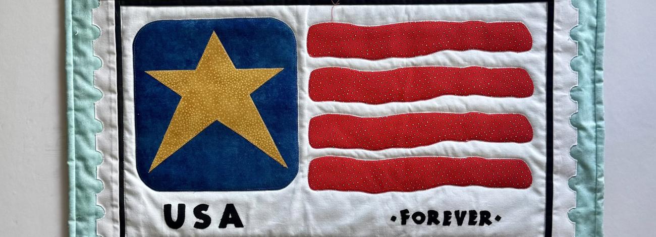 Quilted fabric artwork resembling a USA postage stamp with a gold star, red stripes, and "USA" and "FOREVER" text.