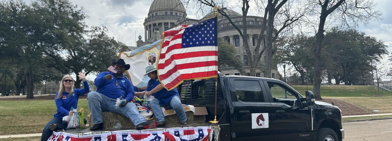 A group of people sit on a truck bed decorated with an American flag and bunting. 