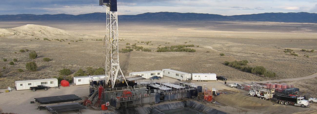 An oil and gas drill rig and pad are seen on an open plain with dark clouds overhead