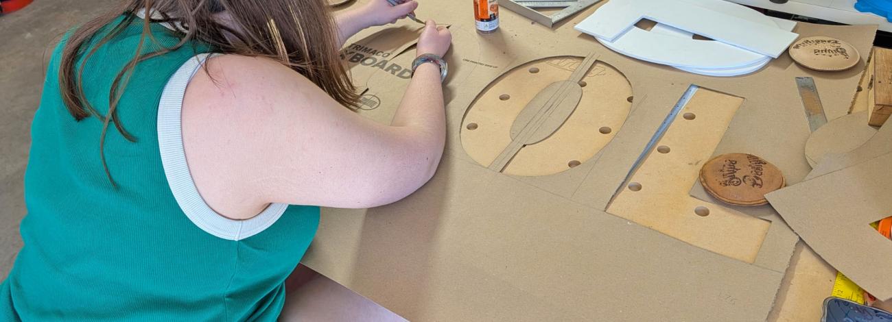 A young woman cuts letters out of a large brown piece of cardboard to make a giant stencil