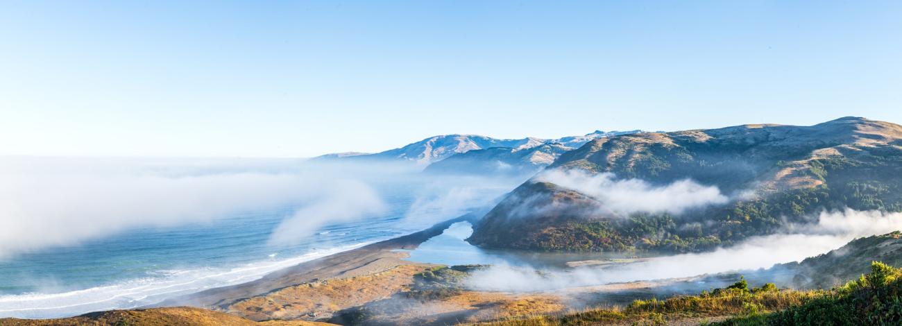 dense fog covers the beach and water over hills near the coast