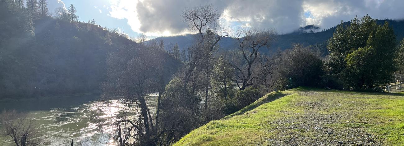 Sun shining down on a river near a green embankment.